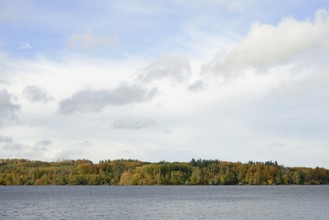 View over Lake Möhnesee, mixed autumn forest on the shore, blue sky, Möhnetalsperre, North