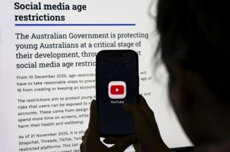 In this photo illustration, a person holds a phone displaying the YouTube app in front of a screen