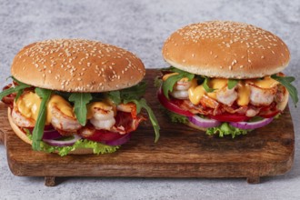Two shrimp burgers and buns with sesame seeds, bacon, lettuce, tomatoes and onions, On a wooden
