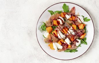 Salad with slices of ripe melon, prosciutto, mozzarella and fresh arugula, decorated with balsamic