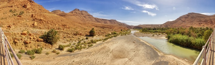 River crosses a barren desert landscape with scattered green plants, Morocco, Achbaro-River Ziz,