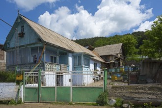 Rural scene with a blue house and several beehives in the foreground, surrounded by nature,