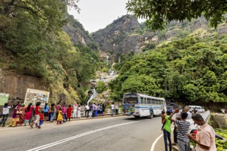 Mountain road with a bus and people looking at a waterfall surrounded by green mountain scenery,