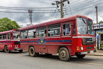 A red bus on a busy street with cloudy skies and power lines, The red buses in Sri Lanka