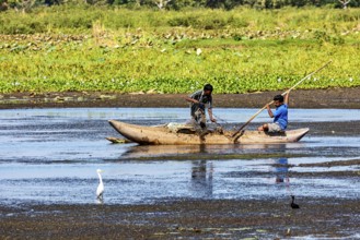 Two children navigate with a paddle through calm waters, nestled in a natural and green landscape,