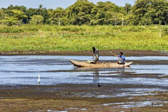Two children paddle in a small boat on a quiet river surrounded by lush greenery and peaceful