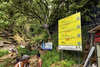 Trail in the jungle with warning signs and people surrounded by trees and rocks, tourists at the