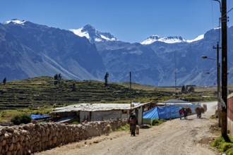 Rural scene with snow-capped mountains and small buildings under blue sky, village in the Andes