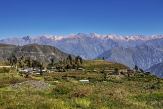 A small village in a mountainous landscape under blue skies with extensive views of the surrounding