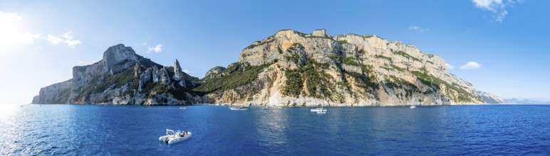 Motor boat off picturesque rocky coast, cliffs with L'Aguglia pinnacle, blue sea and Cala Goloritzé