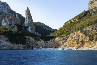 Picturesque rocky coast, cliffs with caves in the morning light, L'Aguglia rock peak, blue sea and