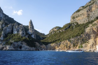 Excursion boat off picturesque rocky coast, cliffs in morning light, L'Aguglia pinnacle, blue sea