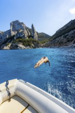 Young woman jumping from a boat into the water, picturesque rocky coast, cliffs with L'Aguglia rock