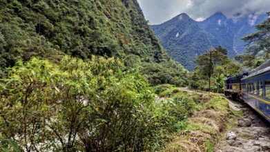 A train travels through a green, mountainous landscape with clouds in the sky, the train through