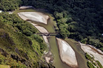 Aerial view of a river with sandbanks and a bridge surrounded by thick forest, view of the Urubamba