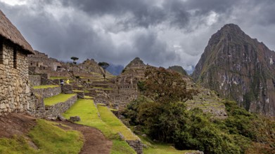 Ruins of Machu Picchu in the foreground against dramatic skies with thick clouds and green areas,