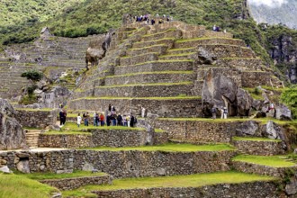 Ruins on terraces full of visitors with surrounding mountains and dramatic clouds, The ruins of the