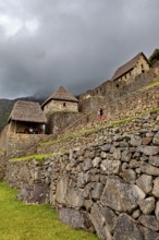 Stone walls and traditional houses against a dramatic, cloudy sky, the ruins of the Inca city of
