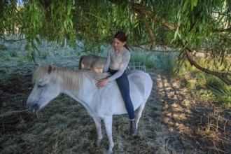 Young girl sitting on her white mare under a willow (Salix), Othenstorf, Mecklenburg-Western