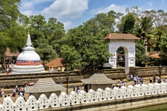A temple complex with a white stupa surrounded by trees and people under clear skies, The Temple of