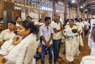 People stand in line in a traditional building, some carry babies, people and pilgrims in the