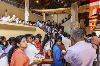 People gather in a decorated building for a religious ceremony with flowers, people and pilgrims at