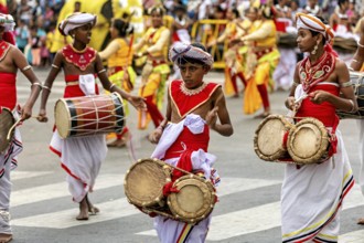 Young drummers in traditional costumes play during a colorful parade on the street, The Perahera