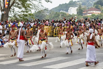 Children move across a street in traditional costumes, spectators watch, The Perahera Parade in