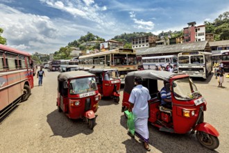 Bustling street scene with tuk-tuks and buses in an Asian city under blue skies, the bus station
