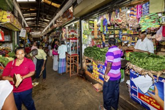 Customers move through a market aisle filled with a wide range of products, retailers in the market