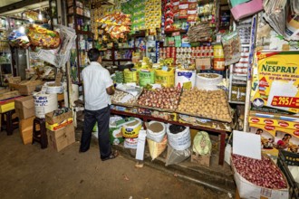 A man in a busy shop surrounded by various colorful packaging and food, dealer in the market halls