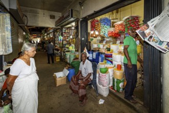 Elderly woman and salesman in a market aisle with colorful goods and packaging, dealer in the