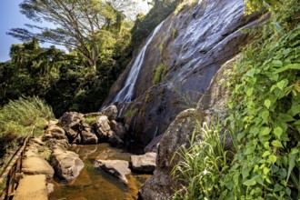 A trail leads past a large waterfall surrounded by lush greenery, waterfall in the highlands near