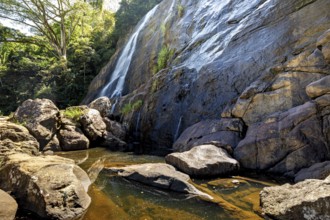 A waterfall flows over large rocks surrounded by trees, waterfall in the highlands near Kandy Sri