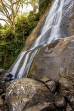 The clear water of a waterfall flows over large rocks, surrounded by green vegetation and tall