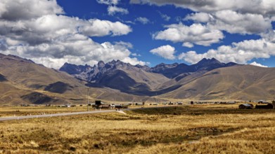 Wide landscape with a road between rolling mountains under a blue sky with clouds, The landscape in