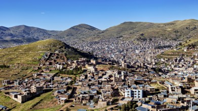 City view of buildings and mountains framed by green hills under a clear blue sky, view of the city