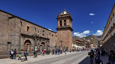 Historic street with impressive bell tower and mountain views, lively with passers-by in clear