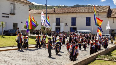 People with colorful flags march through a street with historic buildings under blue skies,