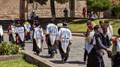 Group of people in white robes with back lettering move down the street during a procession,
