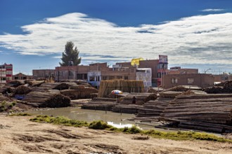 Rural cityscape with stacked wood and water surrounded by buildings under a cloudy sky, tropical