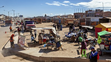 Municipal market with market stalls, people and trucks under clear blue sky, people in the streets