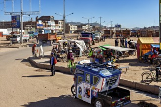 Bustling street scene with tuk-tuk, market stalls and people under bright blue skies, people on the