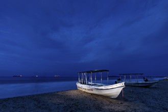 Night landscape with illuminated boat on beach, calm sea and dark sky, traditional boats on