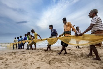 A group works together on the beach to pull a fishing net out of the water, Traditional fishermen