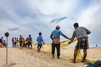 Group of people pulling out a fishing net on the beach, collaborative work at the sea, traditional