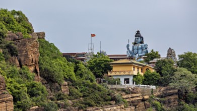 Temple and large Shiva statue on rocky hill surrounded by green vegetation, Koneswaram temple in