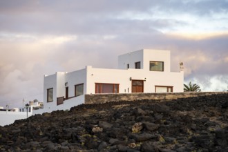 Black coast of volcanic rocks behind typical white houses of the village of La Santa, at sunset,