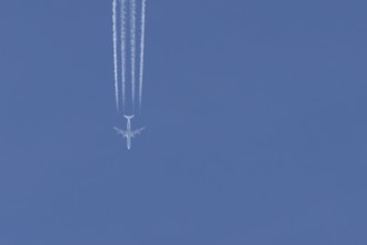 Jet passenger aircraft flying in a blue sky with contrails or vapour trails behind, England, United