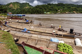 Wooden boats with bananas and motors in front of a mountainous landscape, longboat on a river near